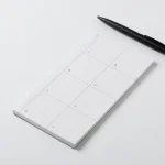 Roda Week Pad lying flat with a pen across it, weekly grid printed on natural shade paper