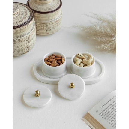 White marble tray holding two lidded trinket bowls filled with nuts, on a light table