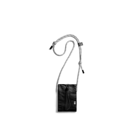 Carbon Black Kick Phone Pocket with its crossbody cord, shown hanging on white