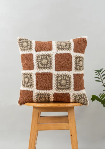Prism Crochet Geometric Fusion Cushion Cover 100% Cotton - Rust by Yellow Dwelling, styled on a light wood stool against a pale wall