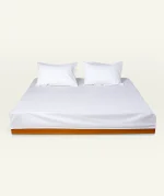 White Plain Bedsheet shown made up on a low wooden platform bed with two matching pillows