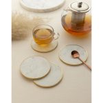 Set of four white marble coasters with brass rims, styled with a glass teapot and cup