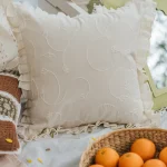 White textured cushion cover with a flanged edge by Yellow Dwelling, styled on layered linens beside a basket of oranges