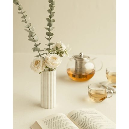 Chic white marble vase holding eucalyptus and white roses, styled with a glass teapot and an open book