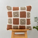 Prism Crochet Geometric Fusion Cushion Cover 100% Cotton - Rust by Yellow Dwelling, styled on a light wood stool against a pale wall