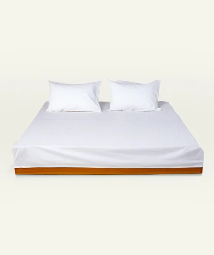 White Plain Bedsheet shown made up on a low wooden platform bed with two matching pillows