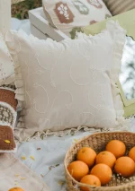 White textured cushion cover with a flanged edge by Yellow Dwelling, styled on layered linens beside a basket of oranges