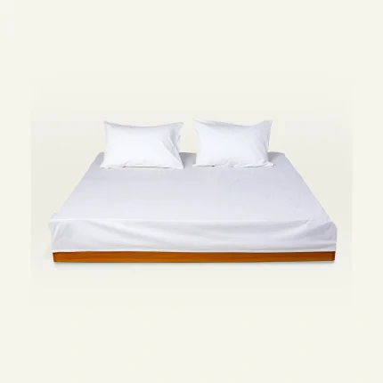 White Plain bed linen shown made up on a low wooden platform bed with two matching pillows
