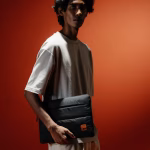 Male model holding black puffy Stria laptop sleeve under arm | KlippiK Kuwait