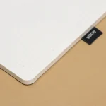 Corner of the Roda Notepad resting on a tan desk mat, dot grid page visible