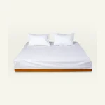 White Plain bed linen shown made up on a low wooden platform bed with two matching pillows